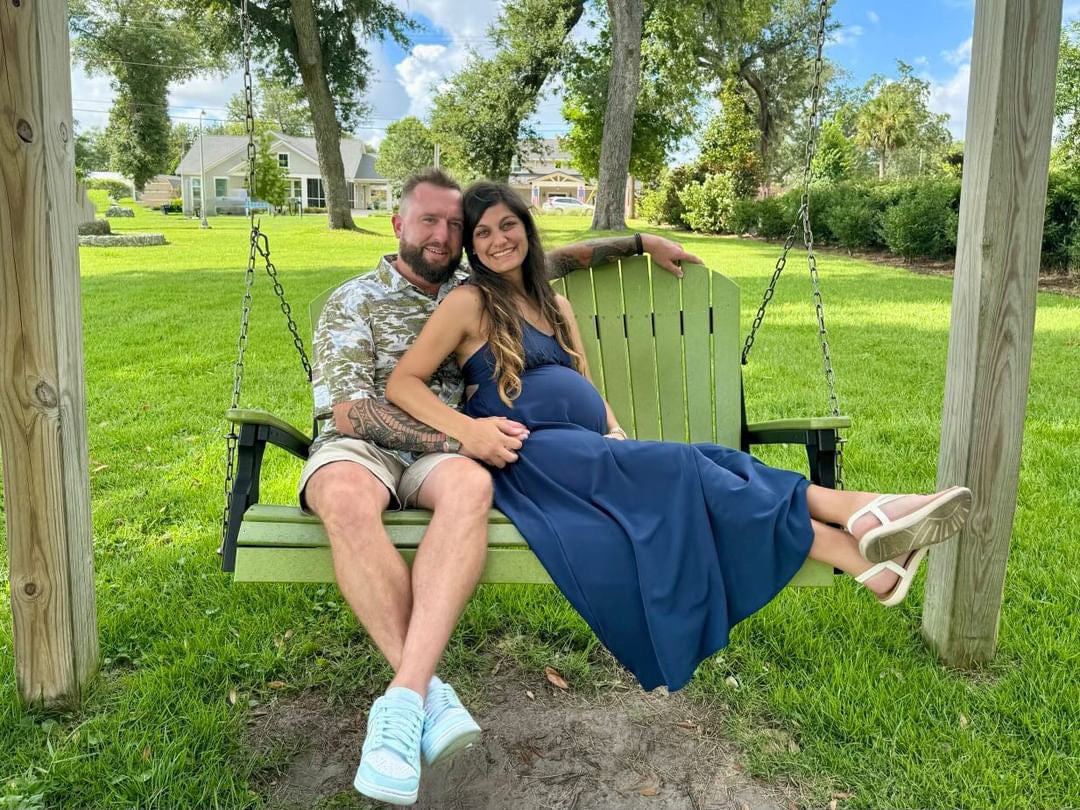 A man wearing the Salt Marsh Floridian Shirt by Okihasi (left side) sitting on a swing with his wife.
